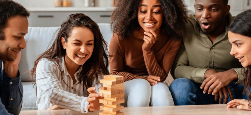 Five friends gathered around a living room table playing jenga
